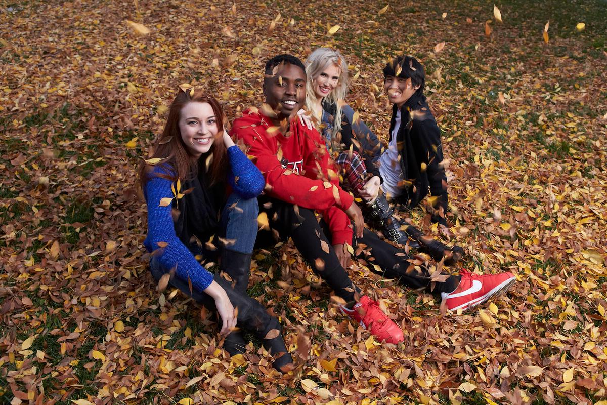 Four people sitting down on the ground covered with a layer of leaves
