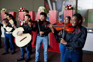 A group of students in a mariachi band play music in front of large red UNLV letters.
