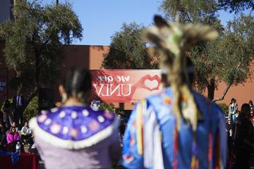 两个穿着土著部落服装的模糊形象出现在校园背景中