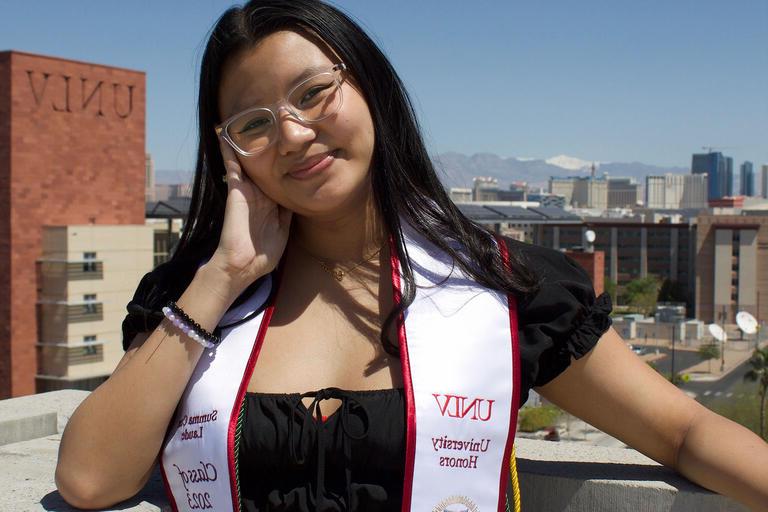 woman posing with UNLV campus in backdrop and graduation stoll