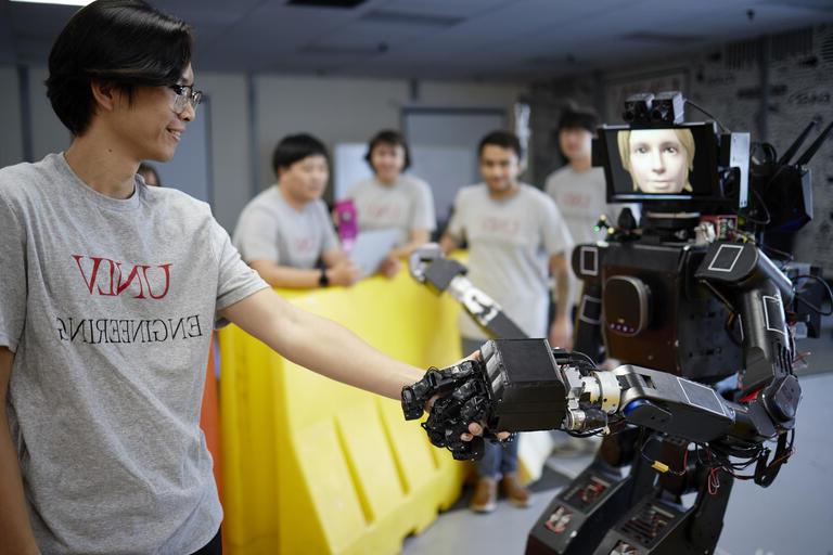 工程学学生与远程呈现的人形机器人握手.