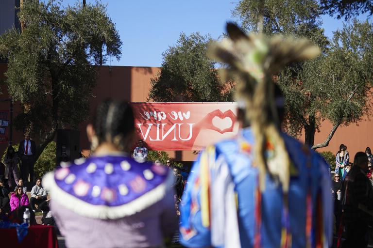 两个穿着土著部落服装的模糊形象出现在校园背景中