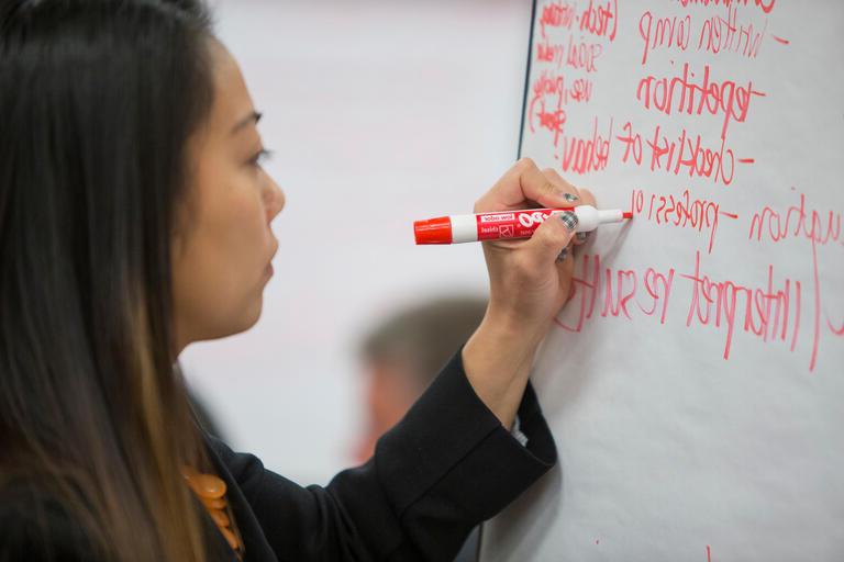 A woman writing notes on a blackboard with an orange marker.
